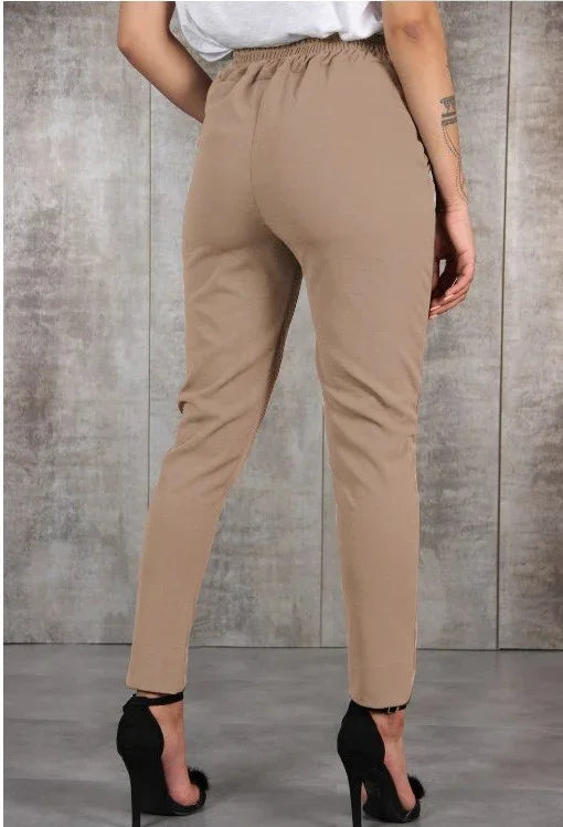 Woman wearing beige slim-fit pants and black high heels against a gray textured background