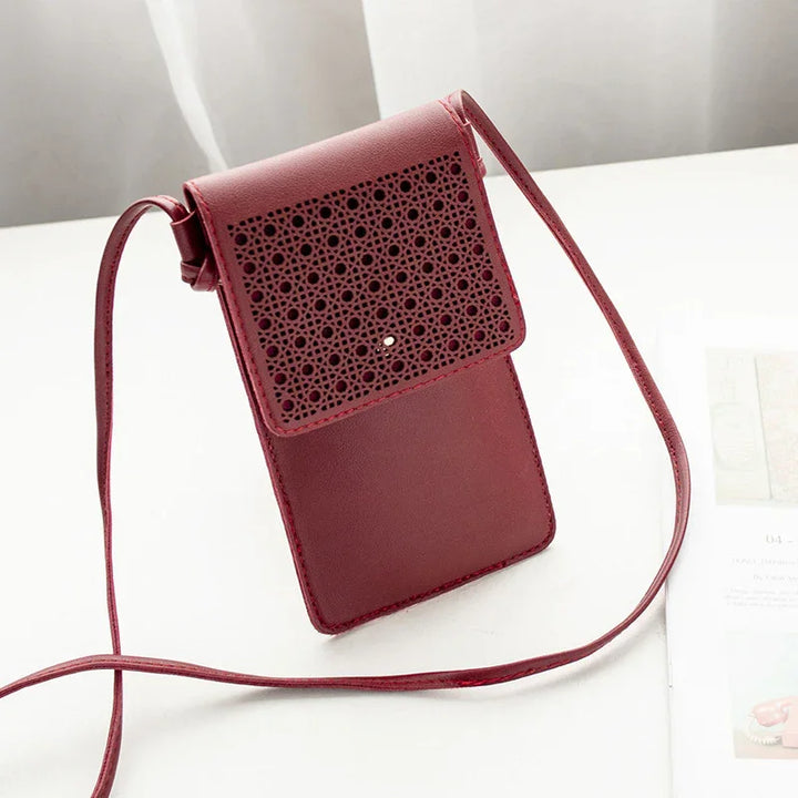 Small maroon crossbody bag with intricate laser-cut floral pattern flap on white surface