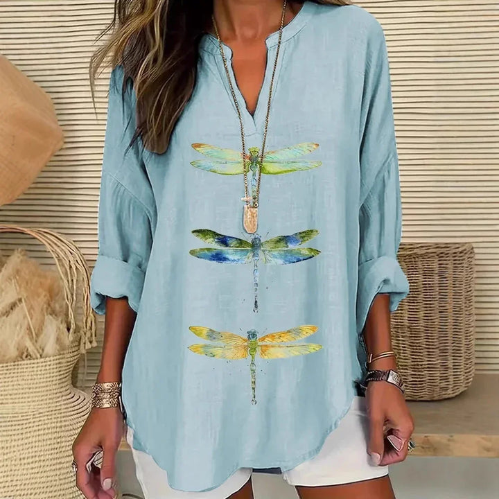 Woman wearing light blue long sleeve shirt with colorful dragonfly prints and white shorts