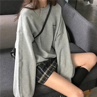 Woman wearing oversized gray sweater and plaid mini skirt sitting on gray sofa