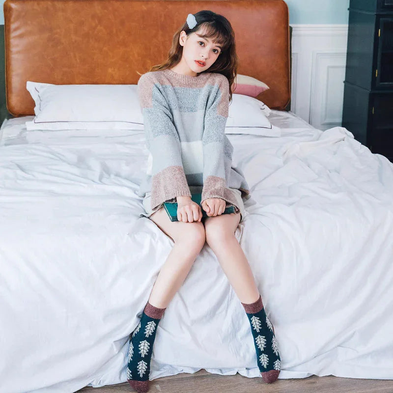 Young woman sitting on bed wearing cozy striped sweater and tree patterned socks in modern bedroom