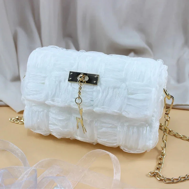 White translucent woven handbag with gold chain strap and deer charm on beige surface