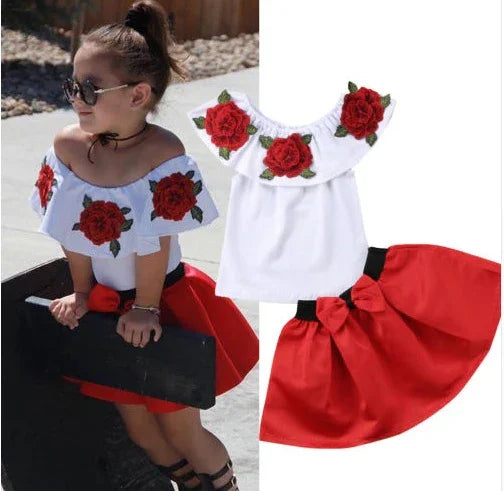 Little girl wearing white off-shoulder top with red rose embroidery and red skirt with bow, outdoor fashion