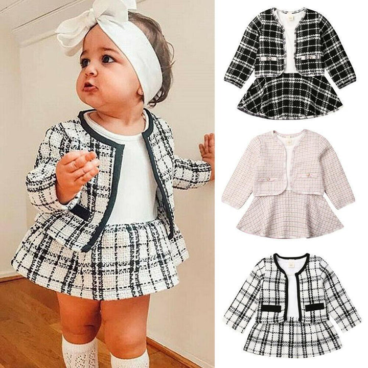 Baby girl wearing black and white plaid jacket and skirt set with white headband and knee-high socks, plaid toddler outfits