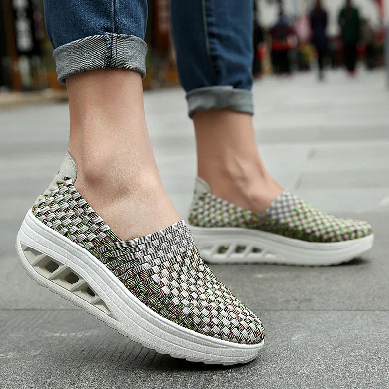 Woven slip-on platform sneakers with thick white soles worn with rolled-up blue jeans on pavement