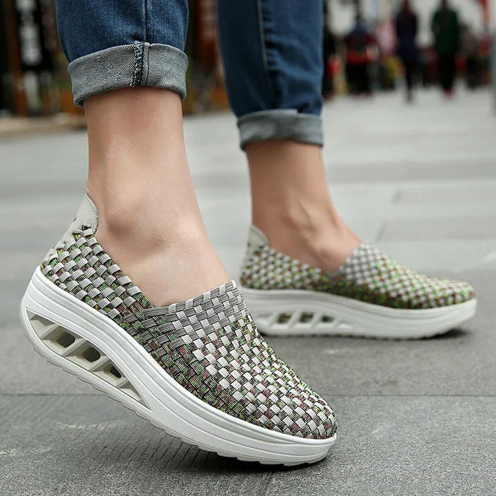Woven slip-on platform sneakers with thick white soles worn with rolled-up blue jeans on pavement