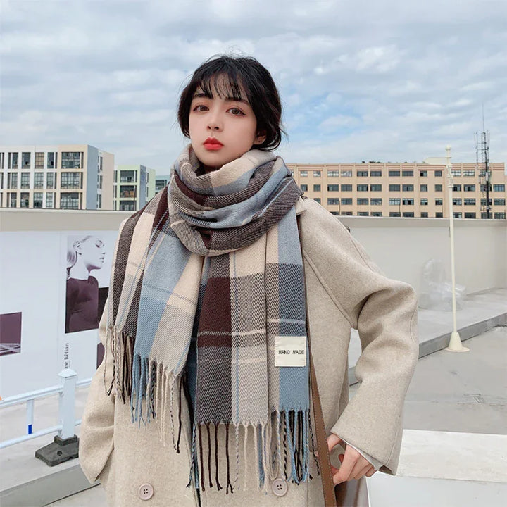 Woman wearing beige coat and blue, brown plaid handmade scarf outdoors in urban setting