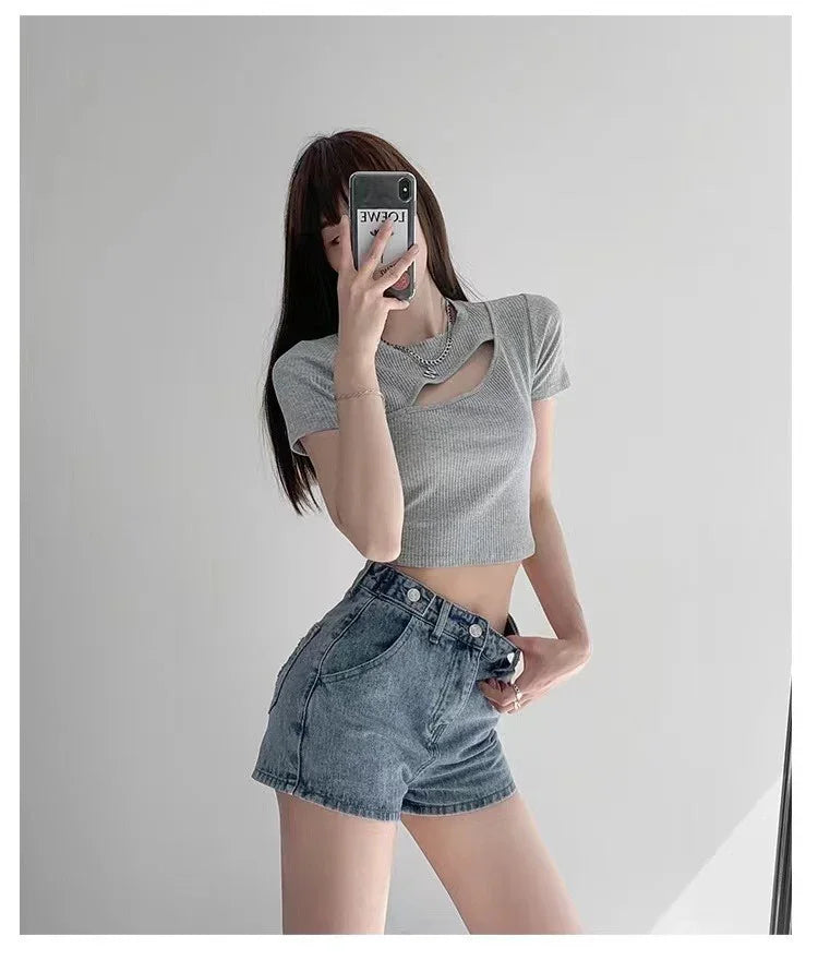 Woman in gray cutout crop top and high-waisted blue denim shorts taking mirror selfie