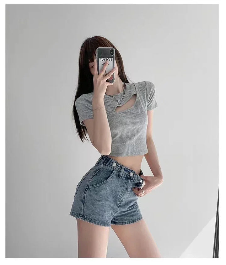 Woman in gray cutout crop top and high-waisted blue denim shorts taking mirror selfie
