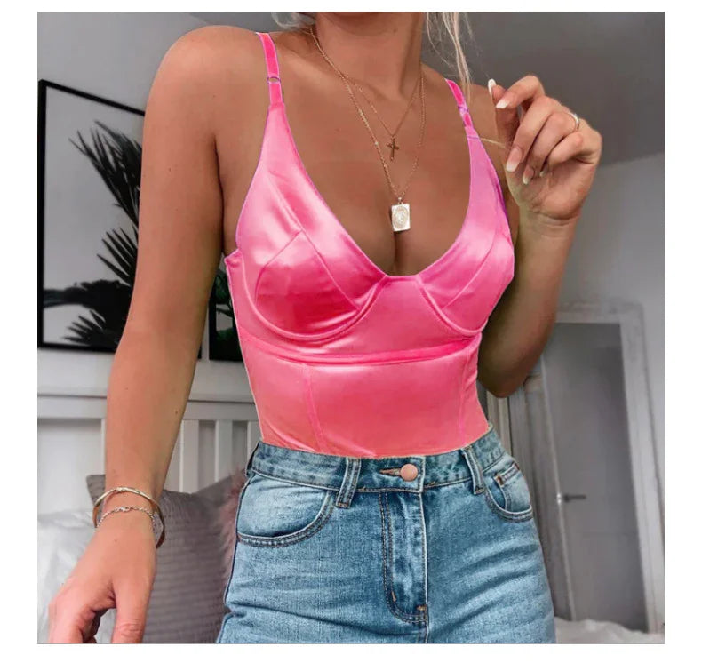 Woman wearing a bright pink satin camisole top paired with high-waisted blue denim jeans in a modern bedroom