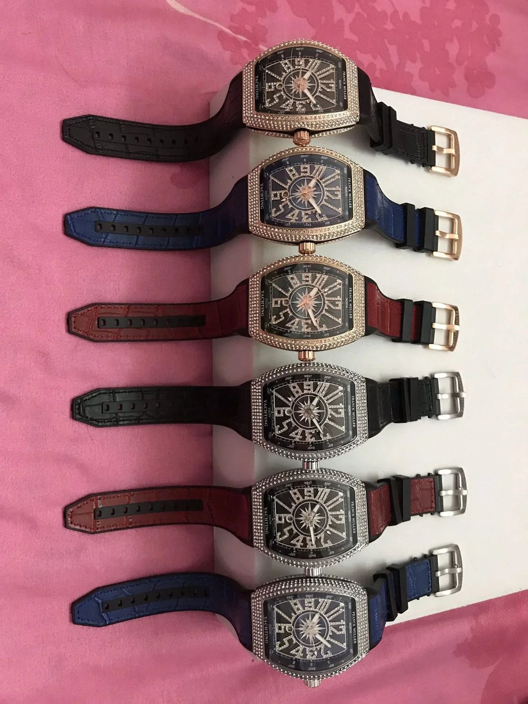 Six luxury Franck Muller Yachting watches with diamond bezels and leather straps in black, blue, and brown on pink background