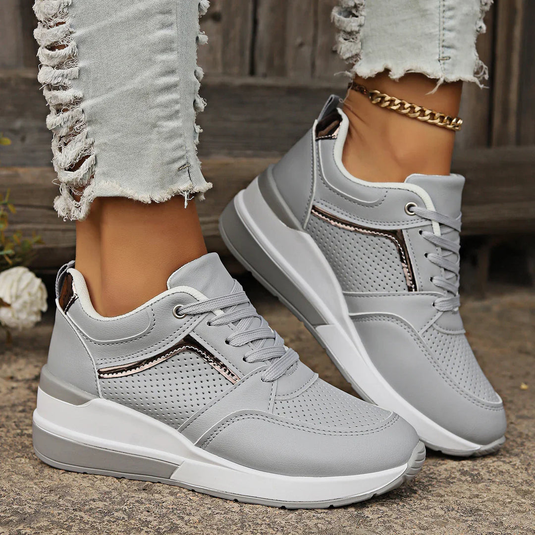 Close-up of gray wedge sneakers with perforated design worn with ripped light denim jeans and gold anklet