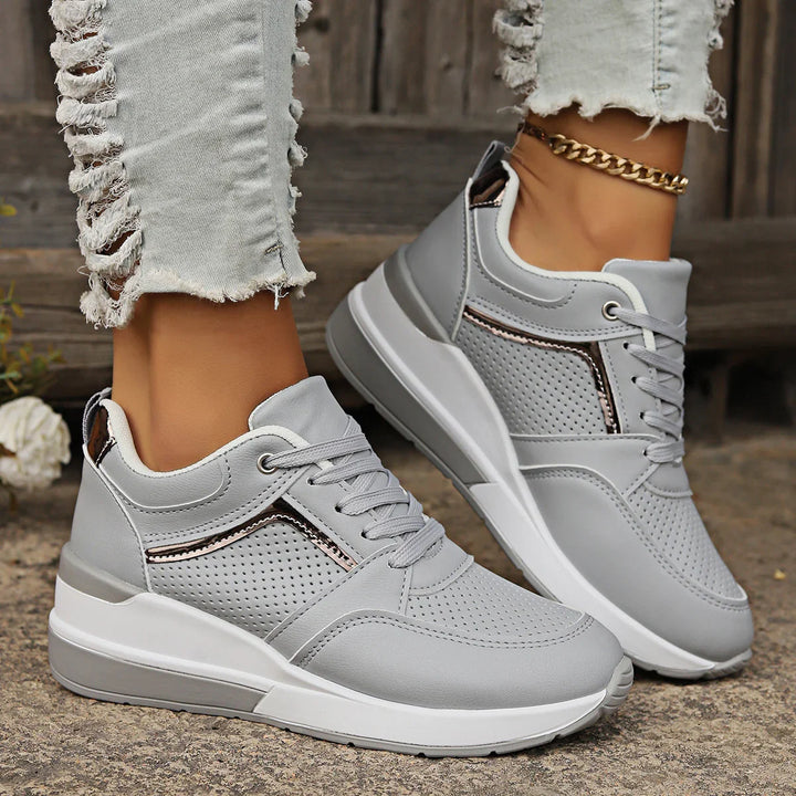 Close-up of gray wedge sneakers with perforated design worn with ripped light denim jeans and gold anklet