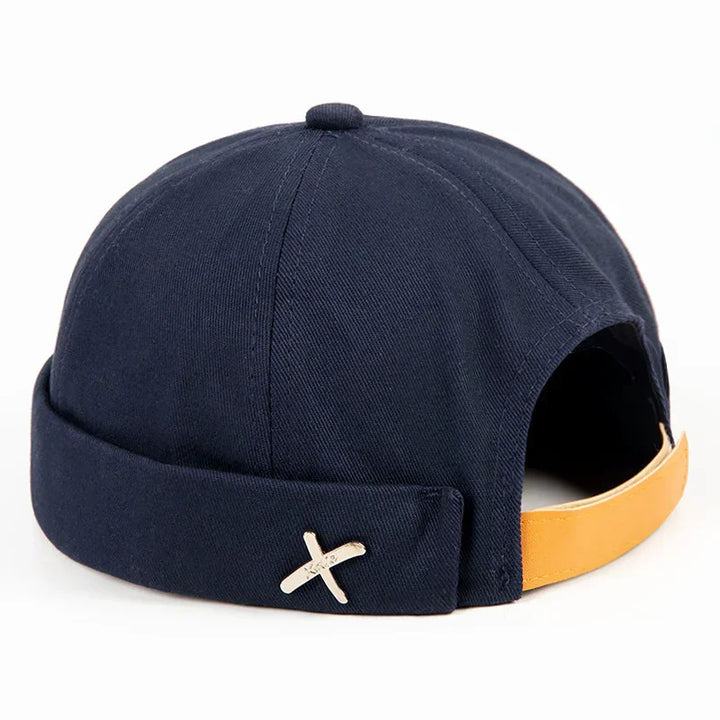 Navy blue docker cap with mustard yellow adjustable strap and silver X emblem on side