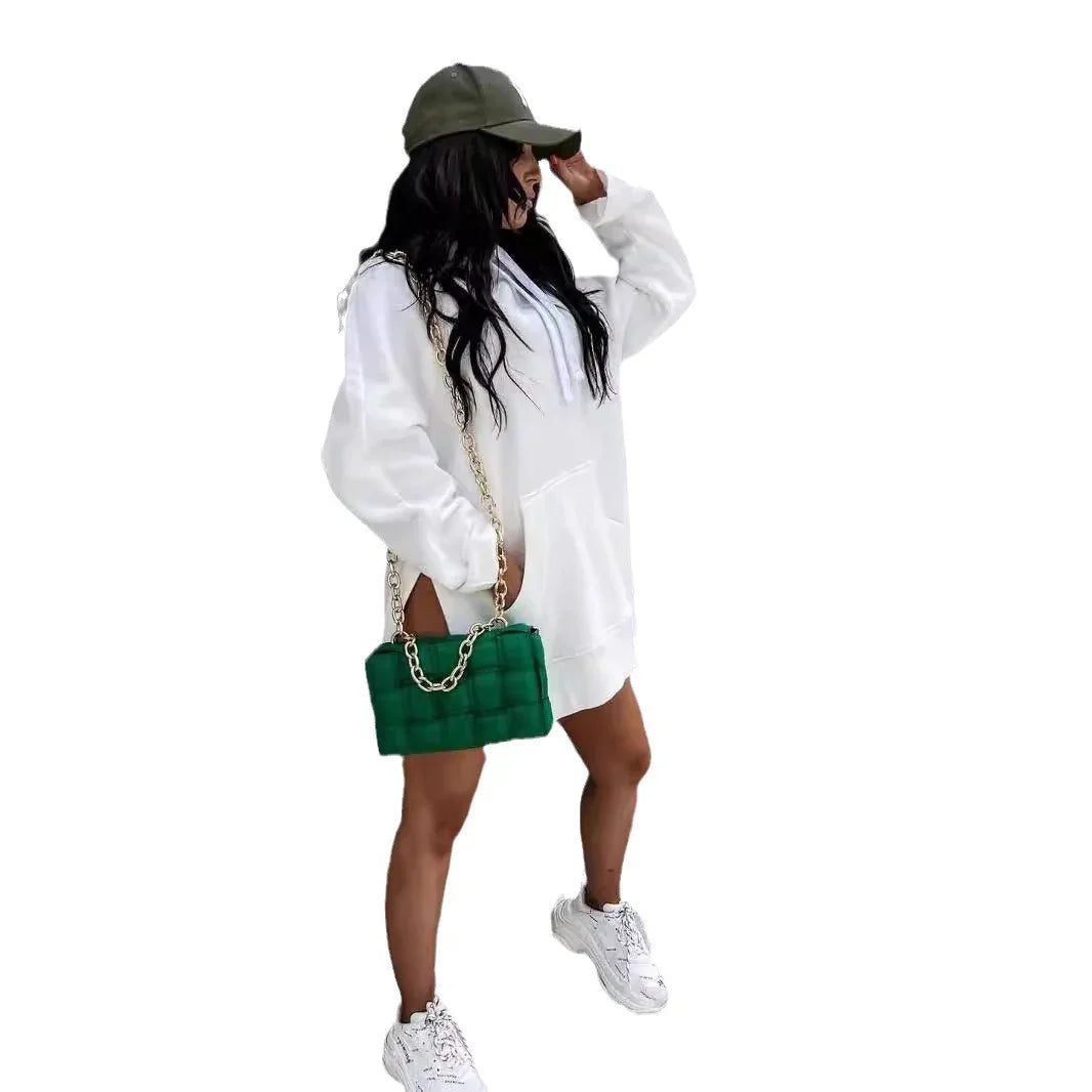 Woman in white hoodie dress wearing green cap and holding green quilted handbag with gold chain
