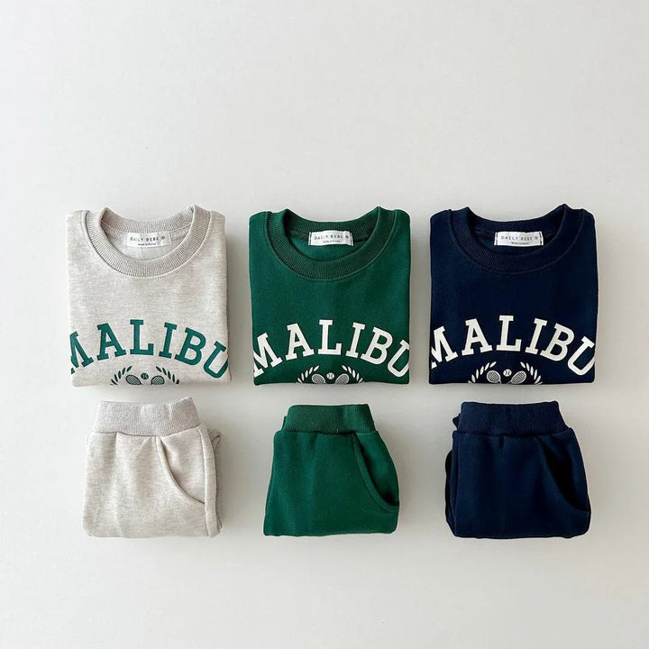 Folded kids sweatshirts and pants sets in beige, green, and navy with Malibu logo