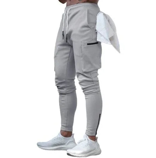 Men's grey jogger pants with cargo pockets, drawstring waist, side zipper, and white sports shoes