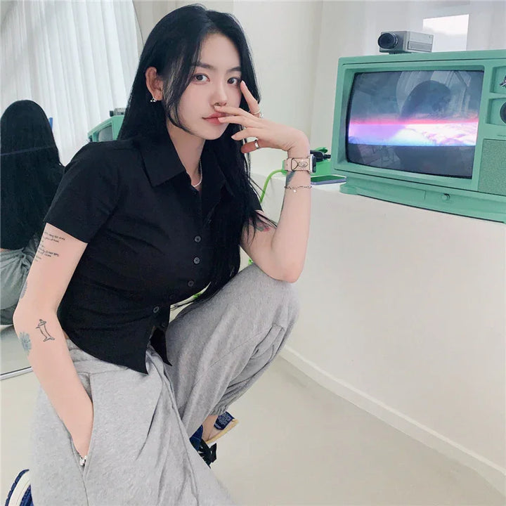 Young woman with long black hair in black shirt and gray pants posing indoors near vintage green CRT TV