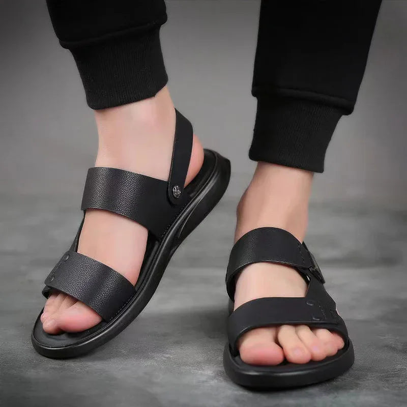 Black leather open-toe mens sandals with adjustable straps worn with black pants on gray floor
