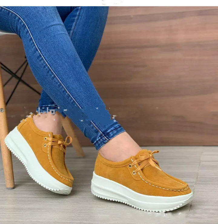 Person wearing mustard yellow platform sneakers with white soles and blue skinny jeans sitting on wooden chair