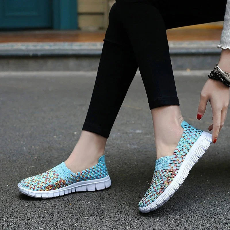 Close-up of feet wearing blue woven slip-on casual shoes with white soles on asphalt