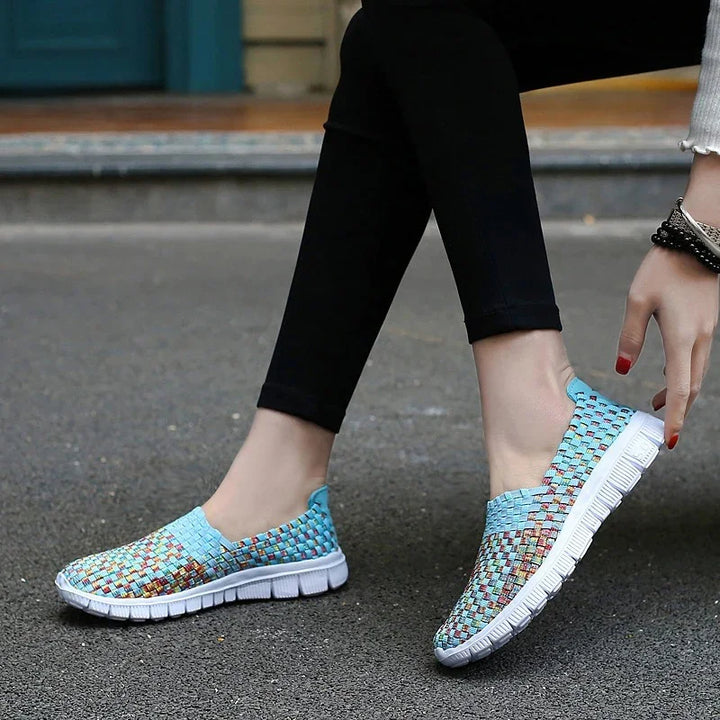 Close-up of feet wearing blue woven slip-on casual shoes with white soles on asphalt