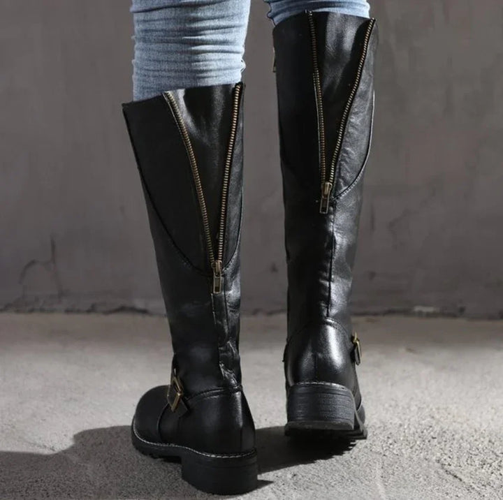 Close-up of black leather knee-high boots with golden zippers and buckles worn with light blue jeans