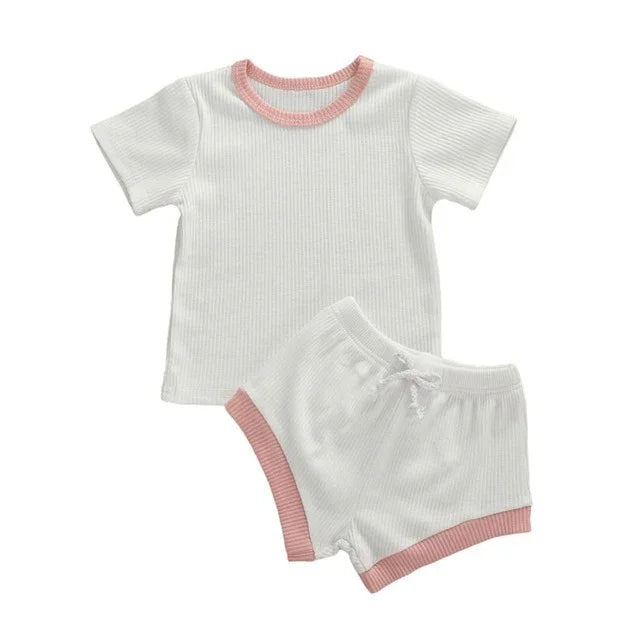 White ribbed toddler outfit with pink trim on collar, sleeves, and shorts edges