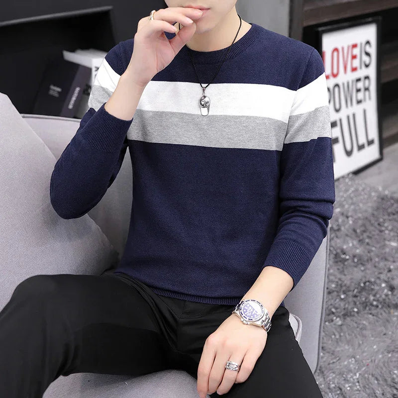 Man wearing navy blue, gray, and white striped sweater with silver watch and rings sitting on gray sofa