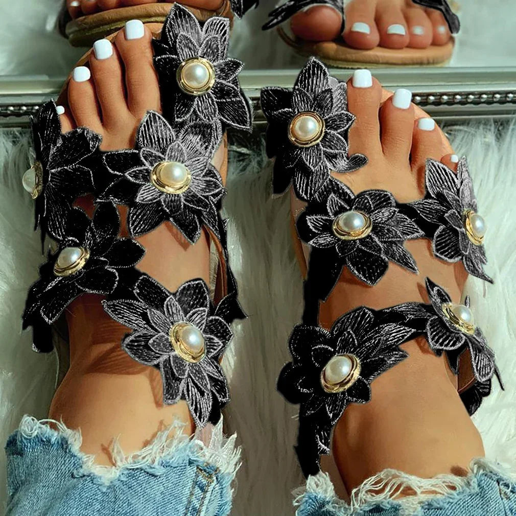 Feet in black floral sandals with pearl centers and white painted toenails on white fur rug