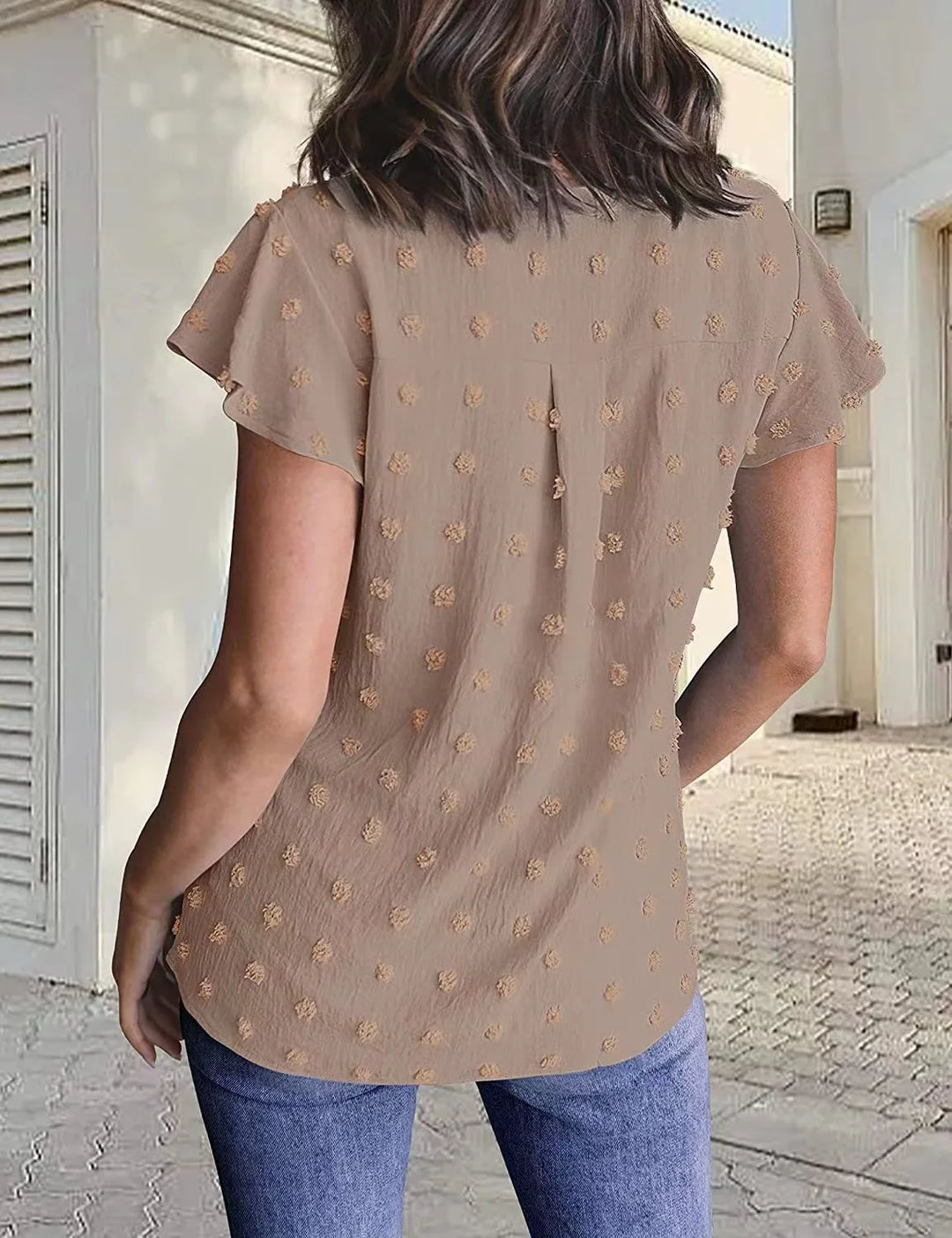 Woman wearing beige short-sleeve blouse with textured polka dots and blue jeans in patio setting