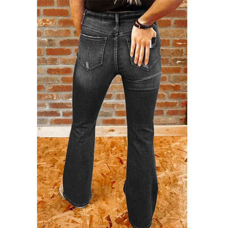 Back view of woman wearing black flare jeans with distressed pocket details against brick wall