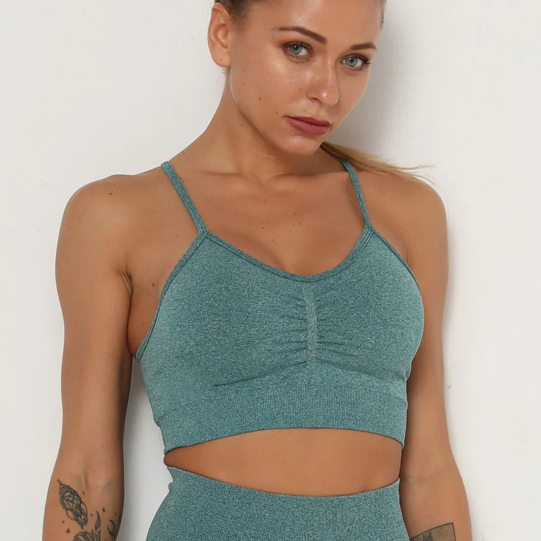 Fit woman wearing teal seamless sports bra and high-waisted leggings against white background