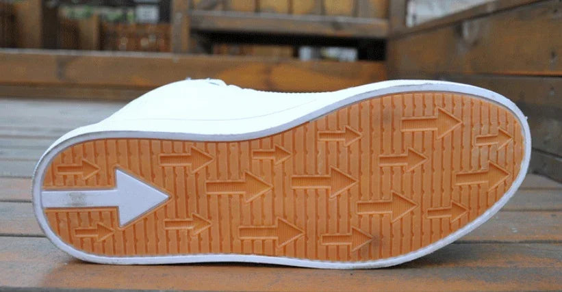 Close-up of white sneaker sole with orange tread featuring multiple arrow patterns on wooden surface