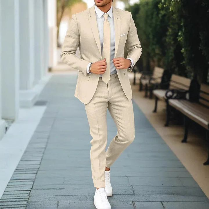 Man wearing beige slim fit suit with matching tie and white sneakers walking on urban pathway