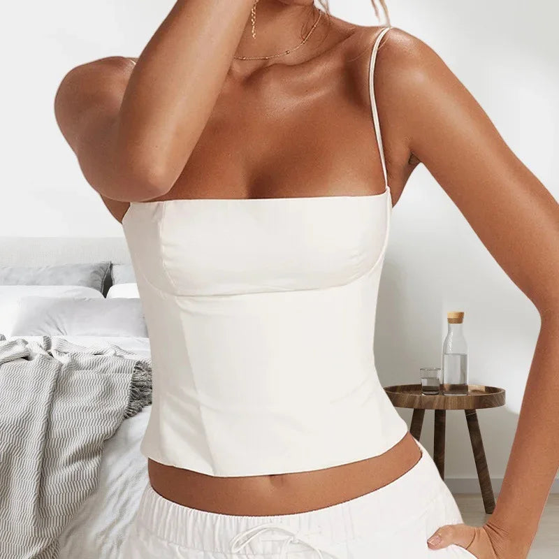 Woman wearing white camisole top and white drawstring pants in a bedroom with wooden side table
