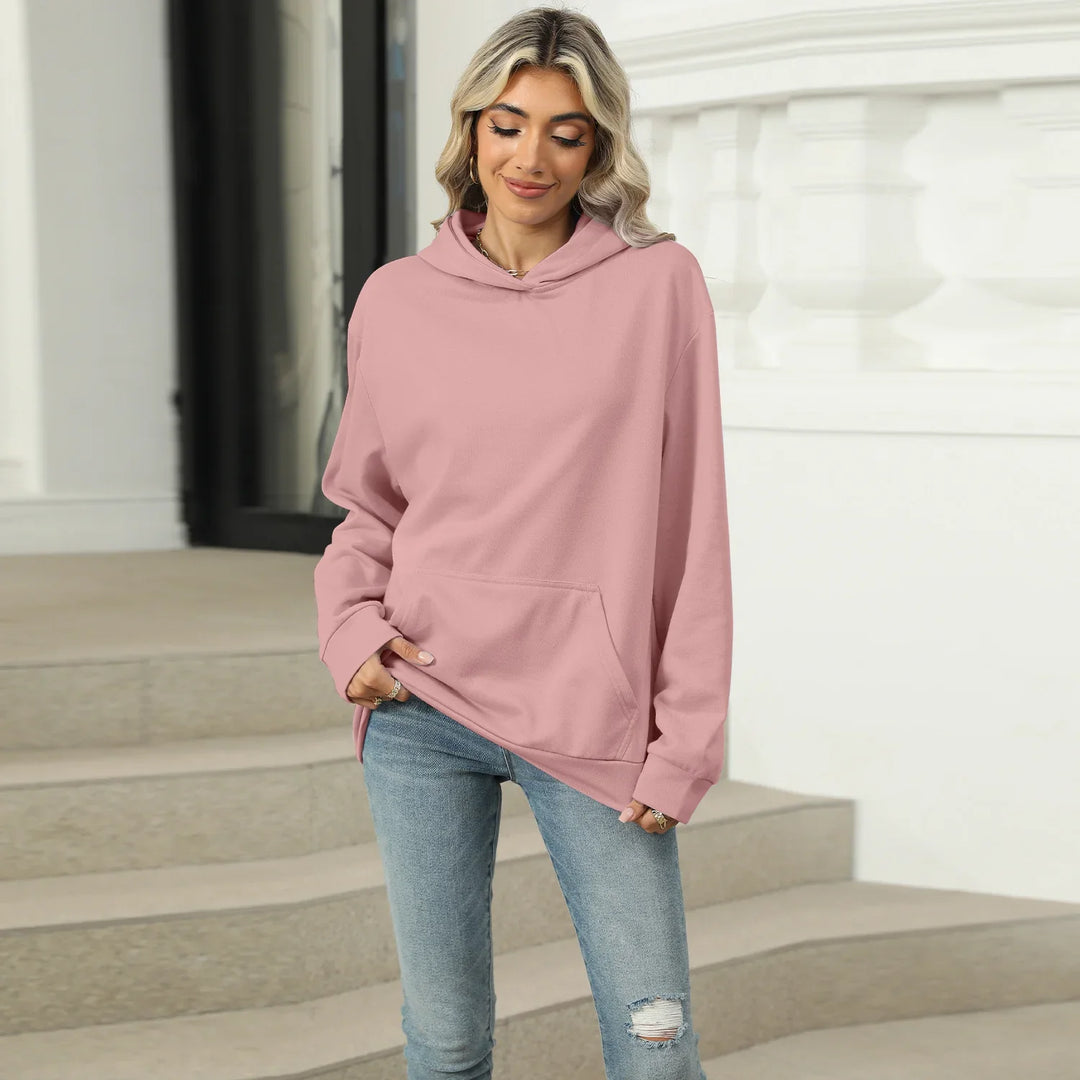 Smiling woman wearing a pink hoodie and ripped light blue jeans, standing by outdoor stairs