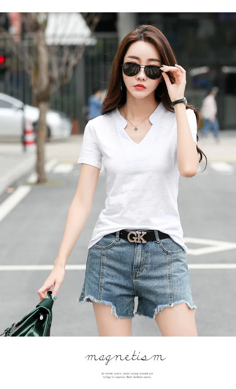 Woman wearing white V-neck T-shirt, denim shorts, black belt with GK buckle, and sunglasses on city street