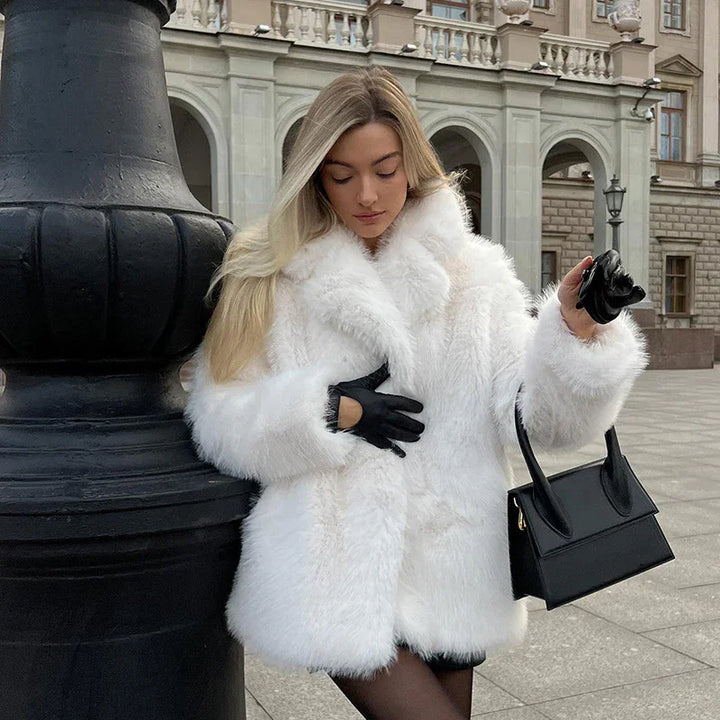 woman wearing stylish white faux fur coat and black gloves holding black handbag in urban setting