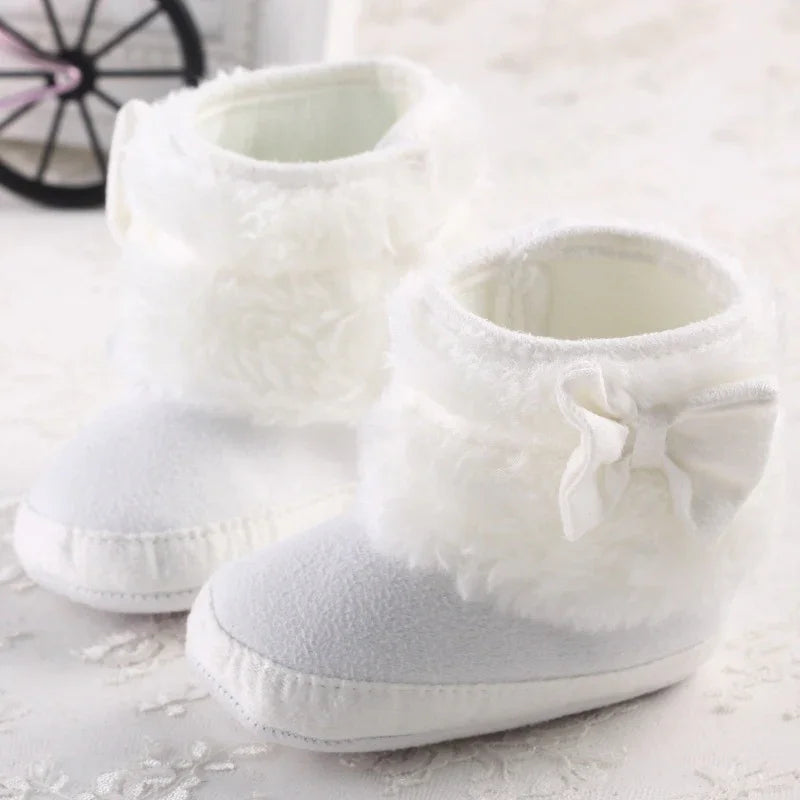 Soft white baby booties with fluffy cuffs and bow detail on a light textured surface