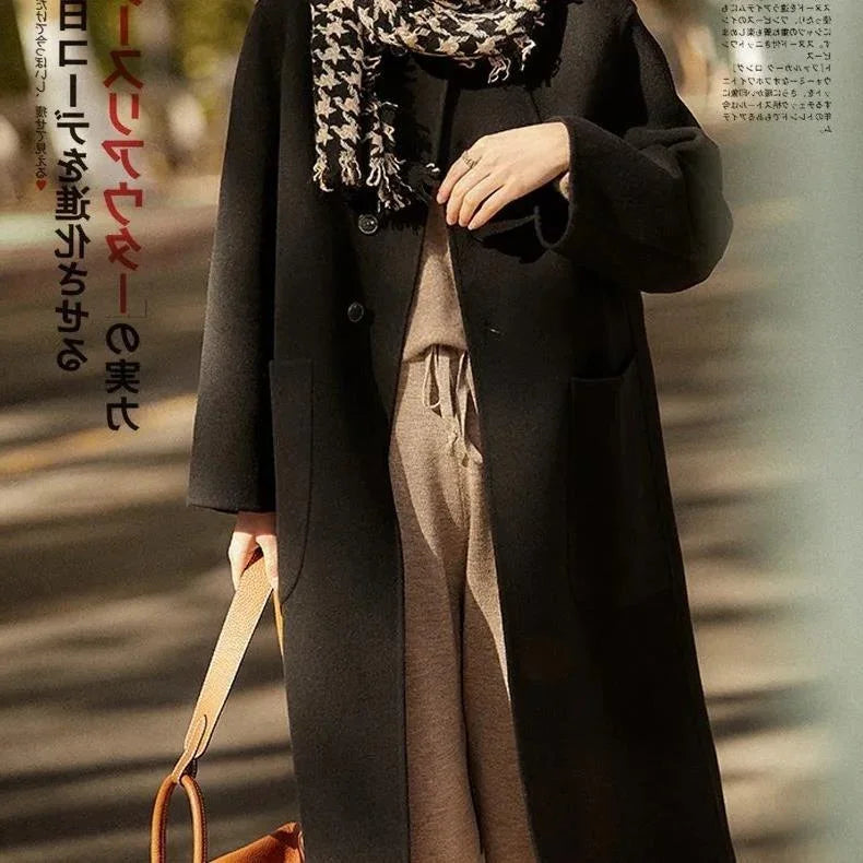 Woman wearing long black coat, beige tie waist pants, houndstooth scarf, holding brown handbag outdoors