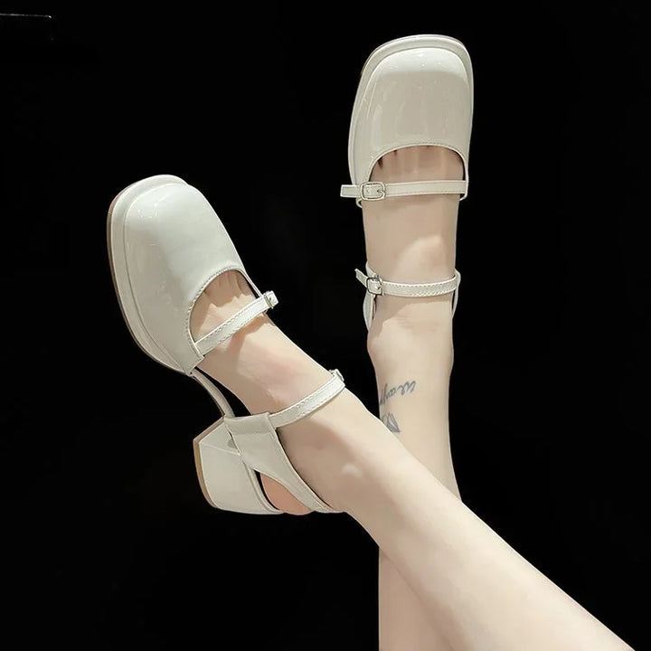 White patent leather Mary Jane heels with ankle straps worn on crossed legs against black background