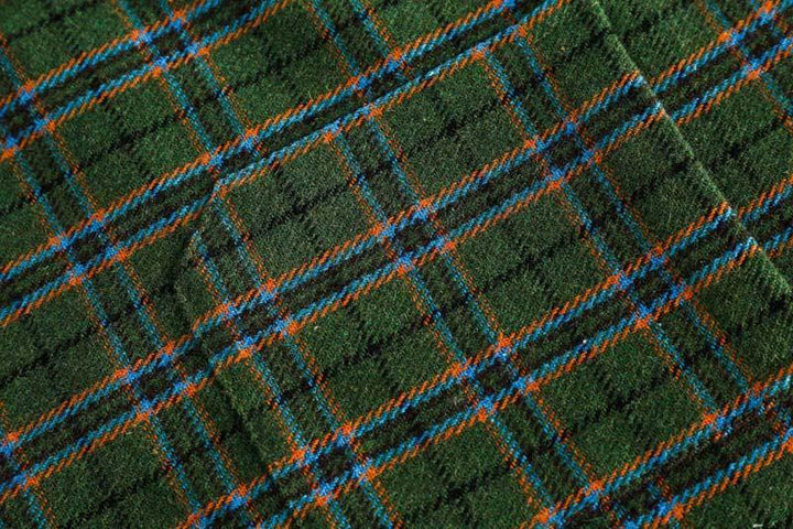 Close-up of green woolen fabric with orange and blue tartan plaid pattern