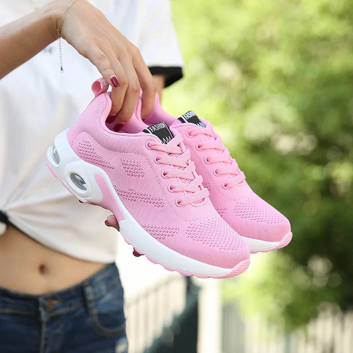 Hand holding stylish pink mesh running shoes with white cushioned sole outdoors