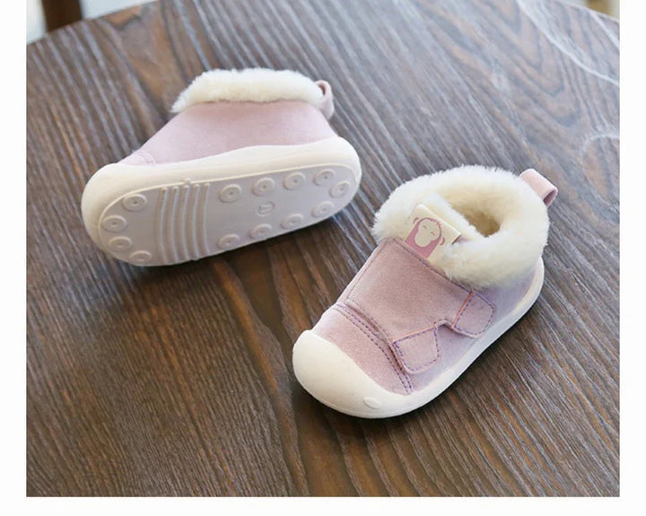 Pink baby shoes with white fleece lining and rubber soles on wooden table