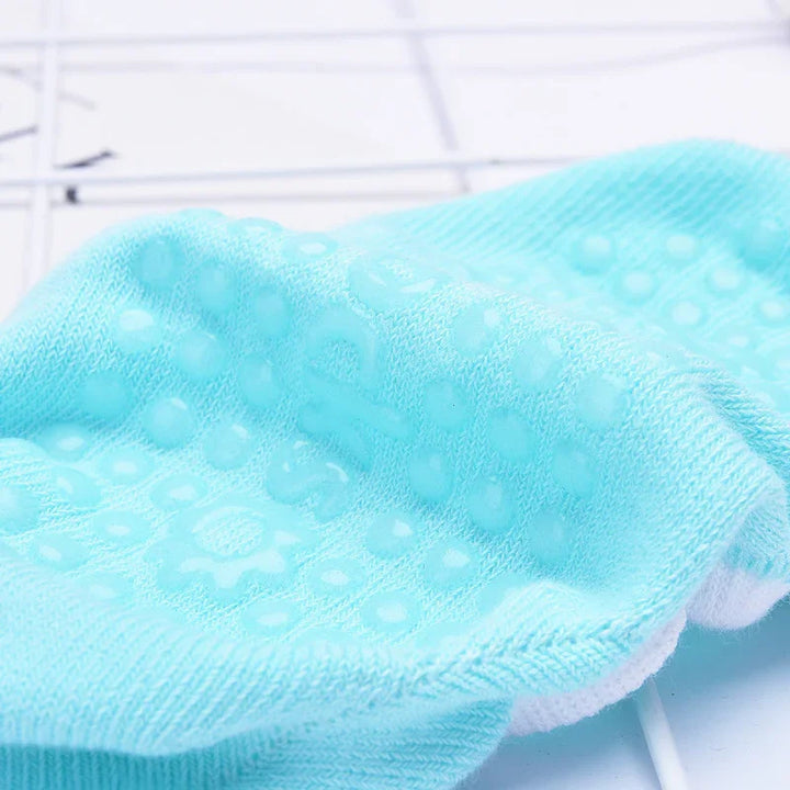Close-up of a light blue non-slip sock with silicone grip dots on a white grid surface
