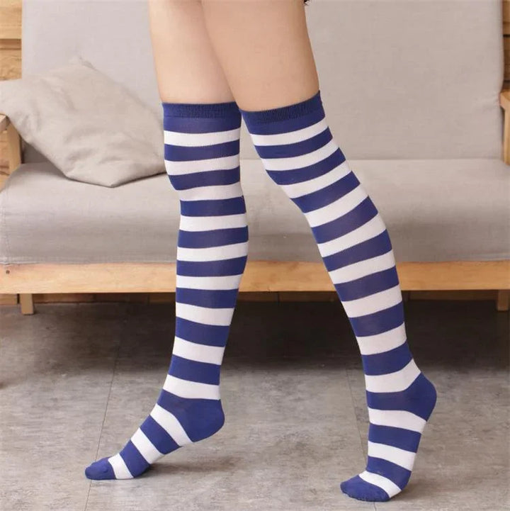 Person wearing blue and white striped knee-high socks standing on gray floor in front of wooden-frame sofa