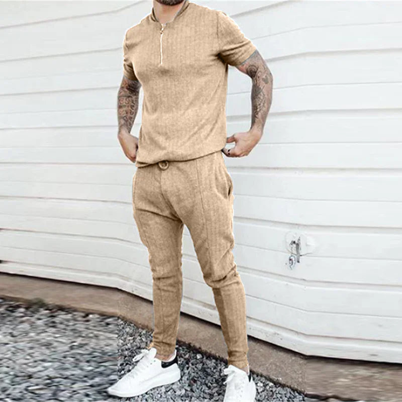 Man wearing beige short-sleeve zip-up shirt and matching jogger pants with white sneakers outdoors