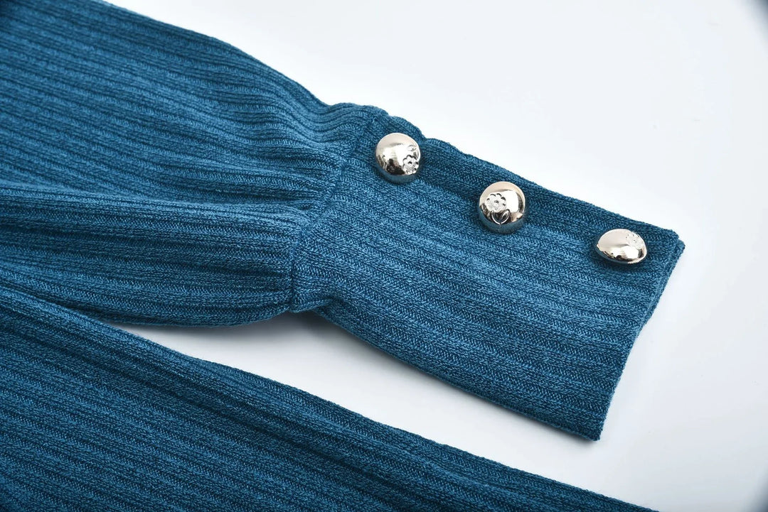 Close-up of a ribbed blue knit sweater sleeve with three decorative silver buttons on white background
