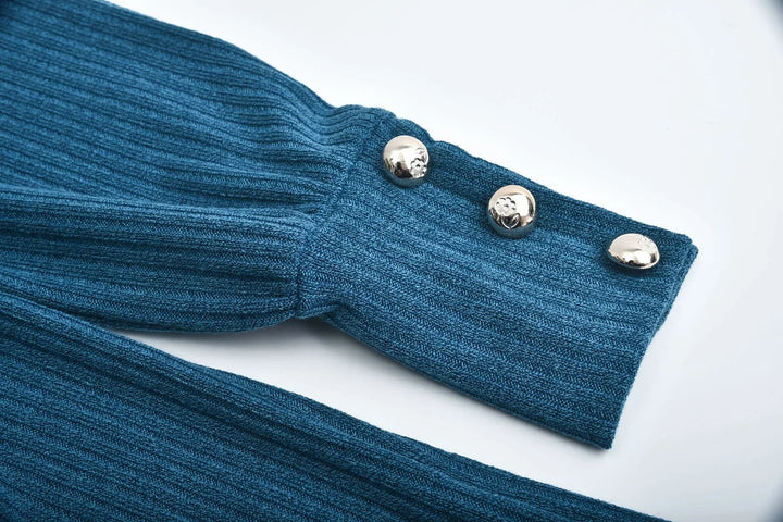 Close-up of a ribbed blue knit sweater sleeve with three decorative silver buttons on white background